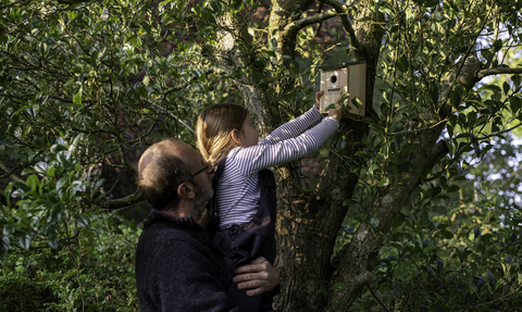 Man holding child as she puts up a bird box