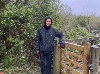 Image of staff member ellie stood in the rain next to the new gate replacement at a reserve 