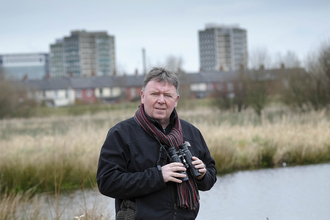 Aidan stands with his binoculars on a reserve