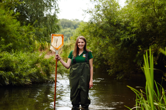 Sophie standing in a river with a net