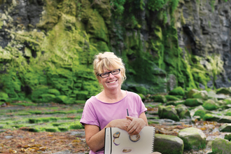 Carol sits on the beach with her sketchbook