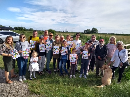 A photo of a group of families at Magor Marsh, holding up their bingo sheets after finding different colours in nature.
