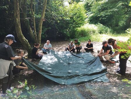 Adults practising knots around a green tarpaulin in the woods