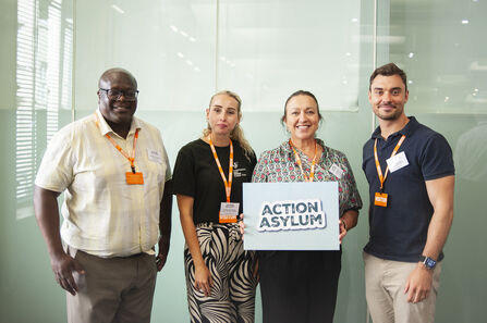 4 people stood together holding a sign that reads 'Action Asylum'